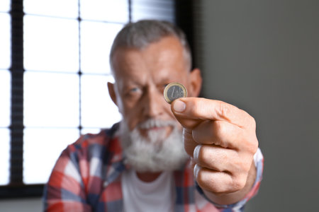 Senior man holding coin indoors, focus on hand. Space for textの写真素材