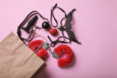 Paper shopping bag with different sex toys on pink background, flat layの写真素材
