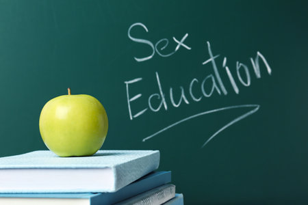 Books and apple near chalkboard with phrase "Sex education"の写真素材