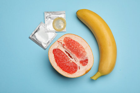 Condoms with banana and cut grapefruit on light blue background, flat lay. safe sexの写真素材