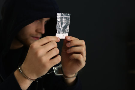 Man detained in handcuffs holding bag with drug against dark background, space for text. criminal lawの写真素材