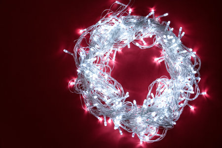 Frame made of glowing Christmas lights on burgundy background, top view. Space for textの写真素材