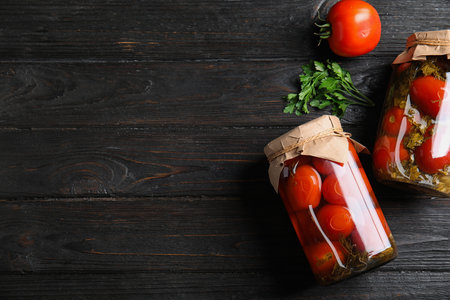 Flat lay composition with pickled tomatoes in glass jars on black wooden table, space for textの写真素材