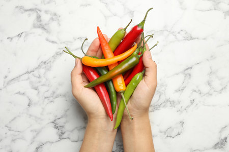 Young woman with handful of different hot chili peppers at marble table, top viewの写真素材
