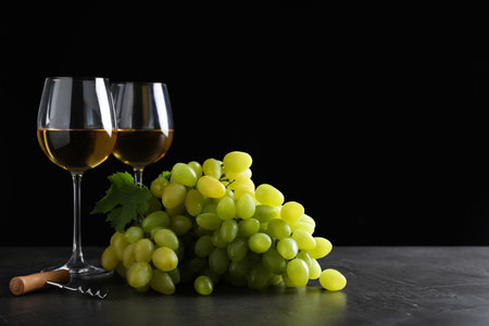 Fresh ripe juicy grapes with wineglasses on gray table against black background, space for textの写真素材