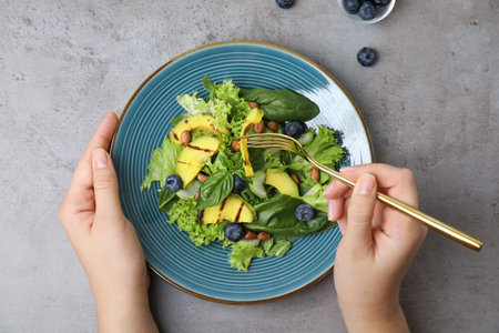 Woman eating avocado salad with blueberries at light gray table, top viewの写真素材