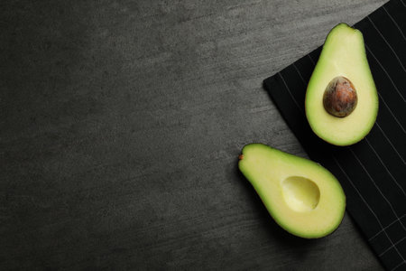 Halves of delicious ripe avocado on gray gray table, flat lay. Space for text