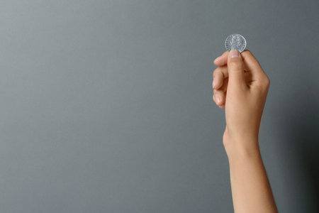 Young woman holding coin on gray background, closeup. Space for textの写真素材