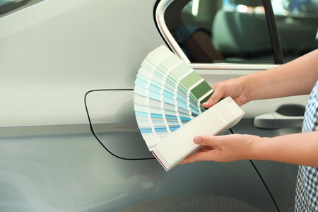 Young woman holding palette with color samples near modern car, closeupの写真素材