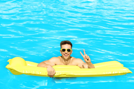 Happy young man with inflatable mattress in swimming pool