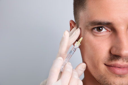 Man getting facial injection on grey background, closeup. Cosmetic surgery