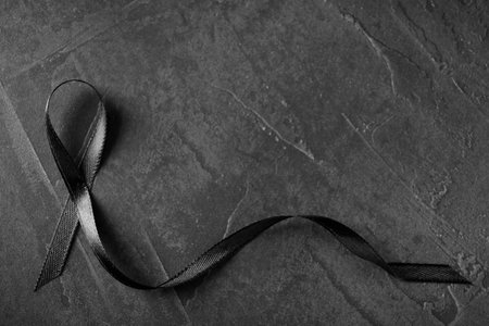 Black ribbon on dark gray stone surface, top view with space for text. funeral symbolの写真素材