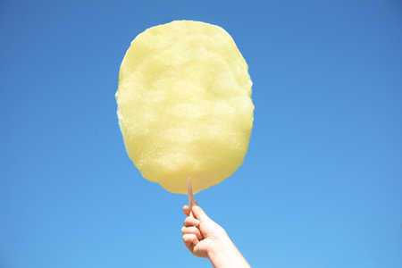 Woman holding white cotton candy against blue skyの写真素材