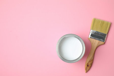 Open can with white paint and brush on pink background, flat lay. Space for textの写真素材