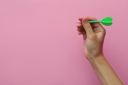 Woman holding green dart on pink background, closeup. Space for textの写真素材