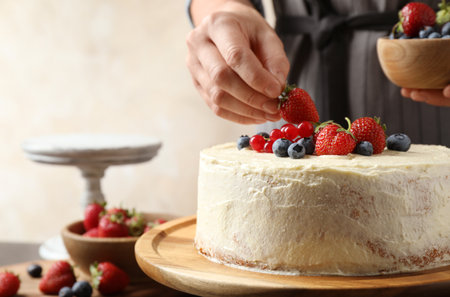 Woman decorating delicious homemade cake with fresh berries at table indoors, closeupの写真素材