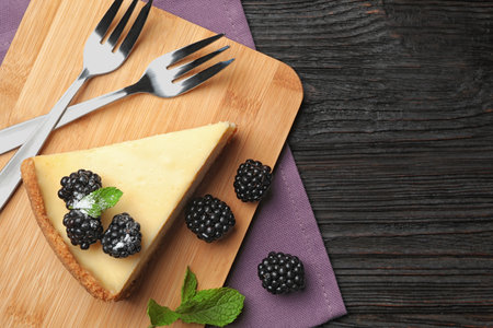 Piece of delicious cheesecake with blackberries on dark wooden background, flat lay. Space for textの写真素材