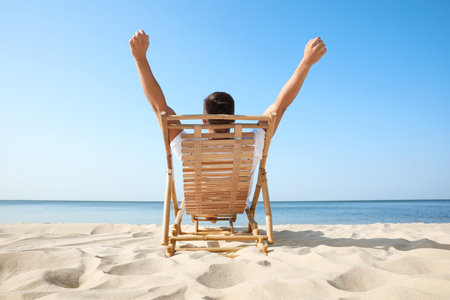 Young man relaxing in deck chair on sandy beachの写真素材