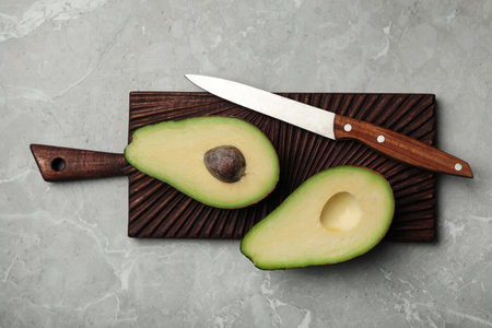 Halves of delicious ripe avocado on gray marble table, top view