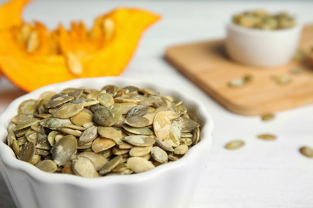 Bowl of raw pumpkin seeds on white table, closeup. Space for textの写真素材