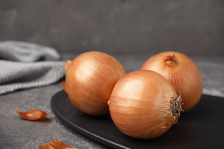 Slate plate with ripe onions on gray table, space for textの写真素材