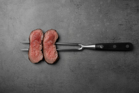 Fork with slices of meat on gray table, top viewの写真素材