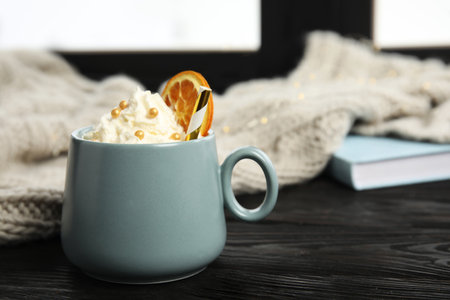 Cup of winter drink with whipped cream and knitted scarf on window sillの写真素材