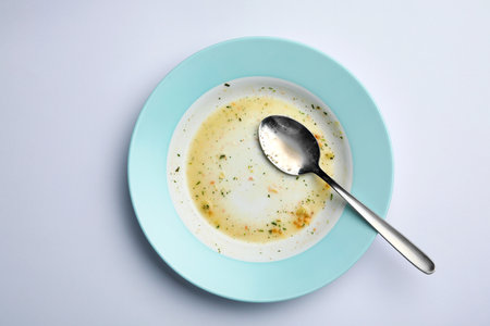 Dirty plate with leftovers and spoon on white background, top viewの写真素材