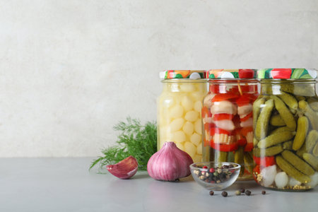 Glass jars with pickled vegetables on gray table against light background. Space for textの写真素材