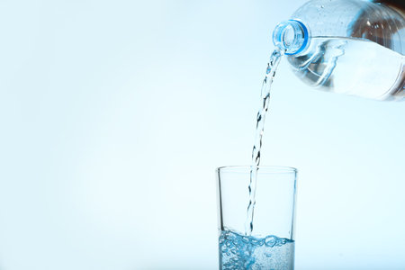 Pouring water from bottle into glass against blue background. Refreshing drinks