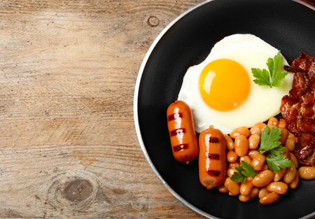 Frying pan with traditional English breakfast on wooden table, top view. Space for textの写真素材