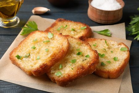 Slices of delicious toasted bread with garlic and herbs on blue wooden table, closeup