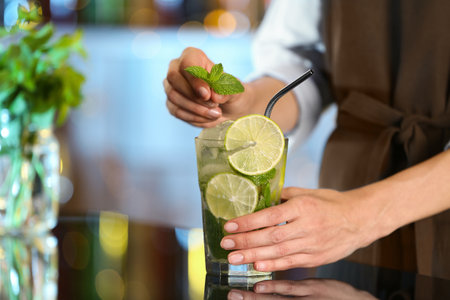 Bartender decorating glass of fresh alcoholic cocktail at bar counterの写真素材
