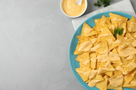 Plate of Mexican nacho chips with sauce on gray table, flat lay. Space for text