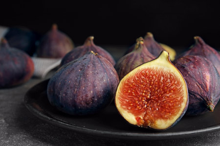 Plate with ripe figs on gray table against dark background, closeup