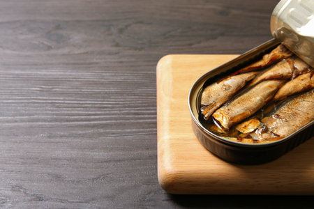 Board with tin can of sprats on wooden table, closeup. Space for textの写真素材