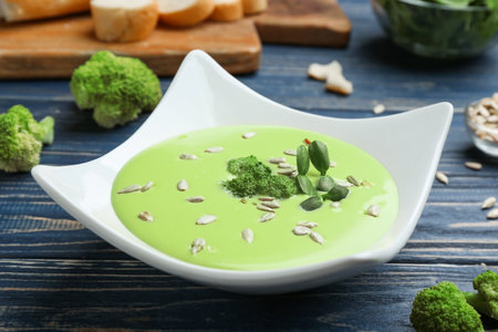Bowl of cheese cream soup with broccoli and sunflower seeds served on blue wooden tableの写真素材