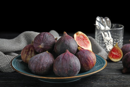 Plate with ripe figs on black wooden table against dark background