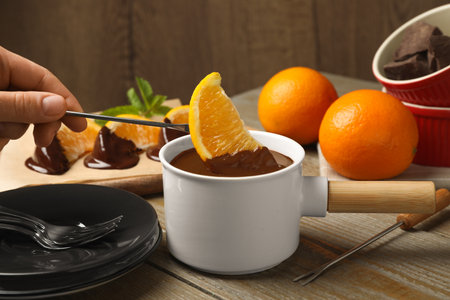 Woman dipping slice of orange into fondue pot with milk chocolate on wooden table, closeupの写真素材