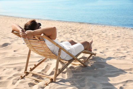 Young man relaxing in deck chair on sandy beachの写真素材