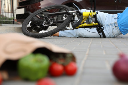 Woman fallen from bicycle after car accident and scattered vegetables on streetの写真素材