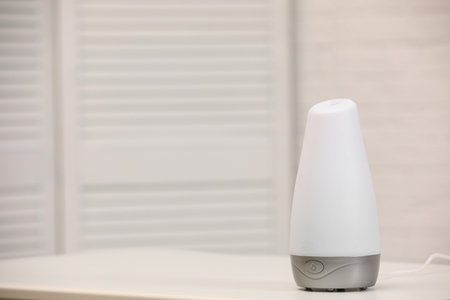 Modern essential oil diffuser on table indoors. Space for text