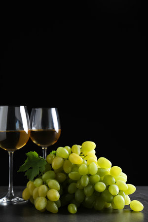 Fresh ripe juicy grapes with wineglasses on gray table against black background, space for textの写真素材