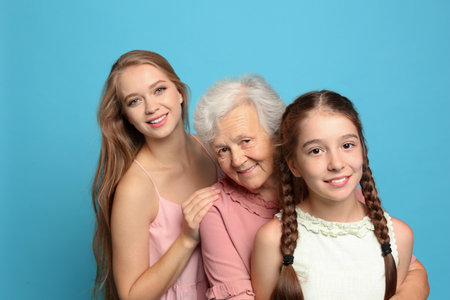 Happy sisters with their grandmother on light blue backgroundの写真素材