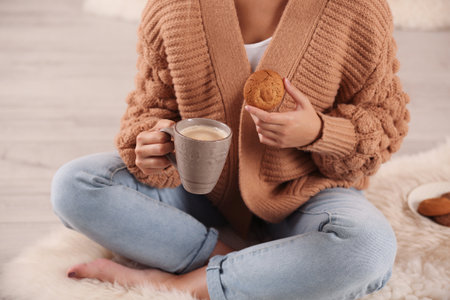 Young woman with cup of coffee and cookie on rug at home, closeup. winter atmosphereの写真素材