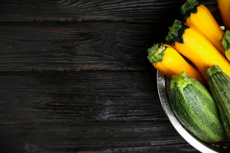 Colander with fresh ripe zucchini on black wooden background, top view. Space for textの写真素材