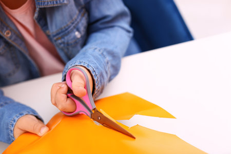Little girl left-handed cutting construction paper at table, closeupの写真素材