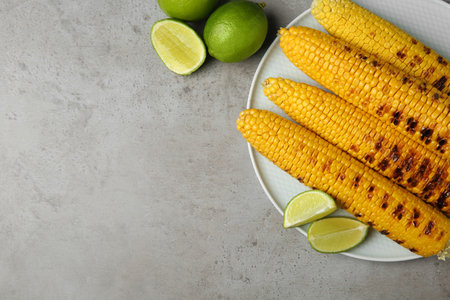 Plate of grilled corn cobs and limes on gray table, flat lay. Space for textの写真素材