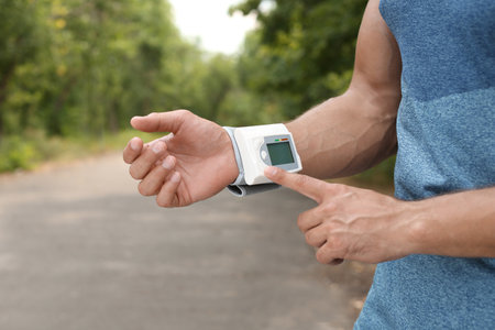 Young man checking pulse with medical device after training in park, closeupの写真素材