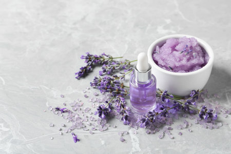 Natural cosmetic oil, bath salt, scrub and lavender flowers on gray marble table, space for textの写真素材